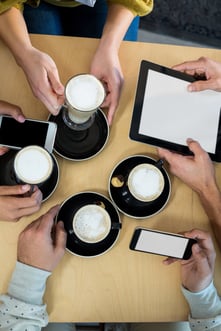 Friends using mobile phone and digital tablet while having cup of coffee in cafx92xA9