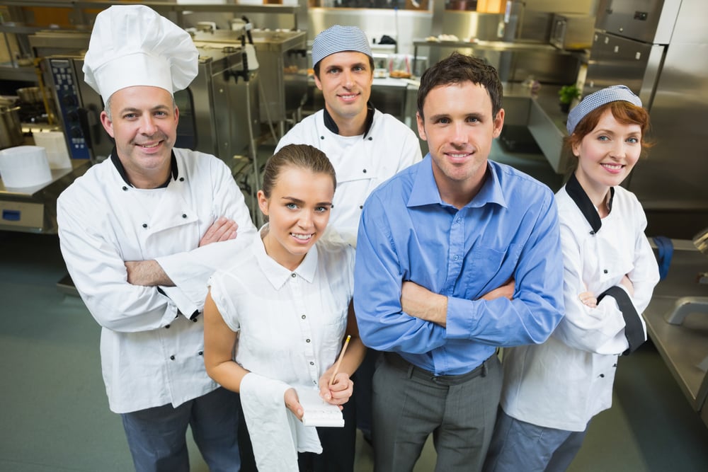 Handsome manager posing with some chefs and waitress in a kitchen